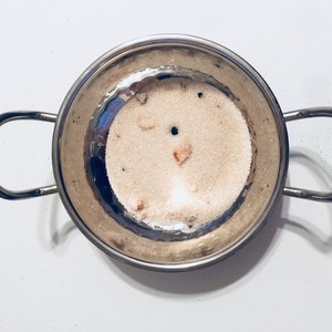 May include: A silver cooking pot with two handles, filled with white sugar and a few brown pieces of fruit.