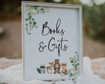 May include: White sign with a wood frame and green foliage border. The sign says "Books & Gifts" in black cursive lettering. There are four woodland animals below the text: a raccoon, a deer, a bear, and a fox.