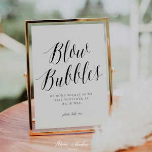 May include: A gold-framed sign with the text "Blow Bubbles" in cursive script. The sign also includes the text "Of good wishes as we exit together as Mr. & Mrs. Please take one" and the company name "Moon Shadow Paperie".