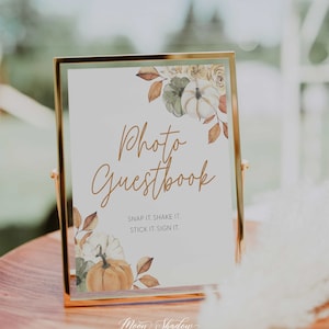 May include: A gold-framed sign with a white background and a watercolor illustration of pumpkins, leaves, and flowers. The sign reads "Photo Guestbook" and "Snap it. Shake it. Stick it. Sign it." Below the text is the logo "Moon Shadow Paperie".