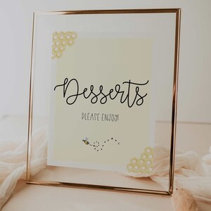 Puede incluir: Un cartel con marco dorado, fondo amarillo y el texto "Postres Por favor, disfrute!" con una pequeña ilustración de abeja y un patrón de panal.