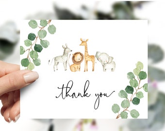 May include: Thank you card featuring a watercolour illustration of a zebra, lion, giraffe, and elephant surrounded by green eucalyptus leaves. The text "thank you" is written in cursive.
