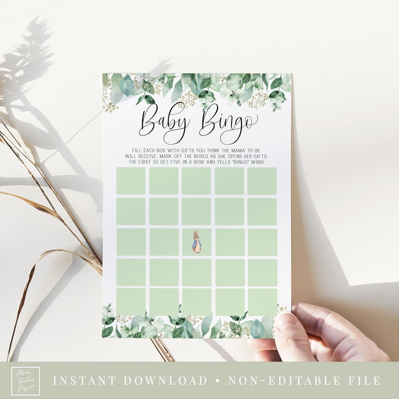May include: A green and gold baby bingo card with a Peter Rabbit illustration. The card has a grid of squares with instructions to fill each box with gifts you think the mama-to-be will receive. The first person to get five in a row and yells "Bingo" wins!