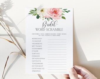 May include: A white bridal word scramble game card with a floral design at the top. The card features the word "Bridal" in elegant script and a list of scrambled words related to weddings. The card is held by a hand.