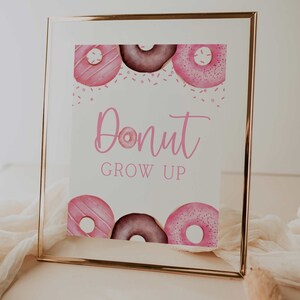 May include: A white sign with pink donuts and the text "Donut Grow Up" in a gold frame.