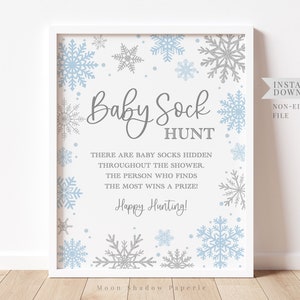 May include: A printable sign for a baby shower game. The sign is white with blue and silver snowflakes and the text "Baby Sock Hunt" with instructions for the game. The text reads: "There are baby socks hidden throughout the shower. The person who finds the most wins a prize! Happy Hunting!"