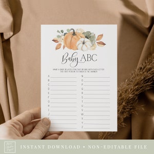 Peut inclure: Une carte de jeu de baby shower imprimable sur le thème de l'automne. La carte a un fond blanc avec une illustration de citrouille et de feuilles d'automne. Le texte sur la carte indique "Baby ABC" et demande aux joueurs de nommer un objet lié à un bébé qui commence par chaque lettre de l'alphabet. La première personne à terminer est la gagnante.