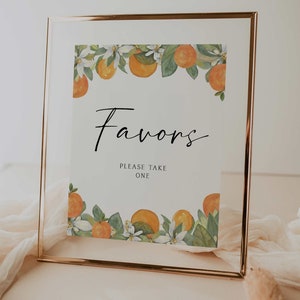 May include: A white sign with a gold frame and a floral border of orange blossoms and oranges. The sign says "Favors" and "Please Take One".