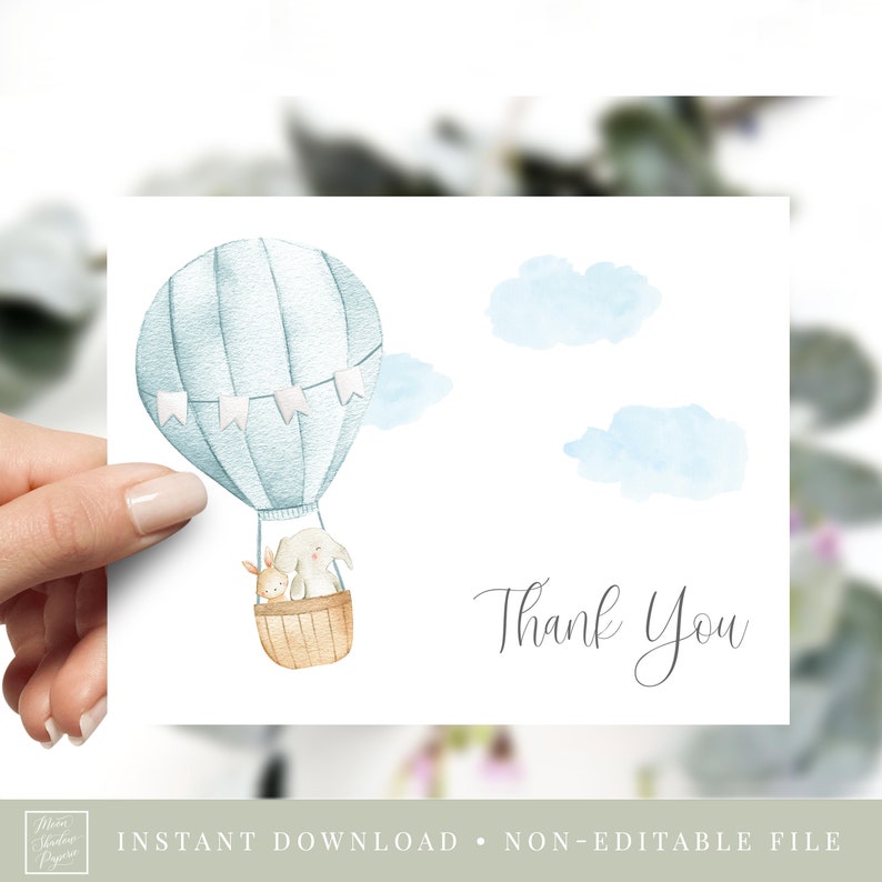 May include: A blue and white hot air balloon with a bunny and a fox inside. The balloon is flying in the sky with white clouds. The text "Thank You" is written in cursive below the balloon.