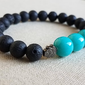 May include: A beaded bracelet featuring black lava stone beads and turquoise-colored beads. A silver-colored accent piece is placed between the black and turquoise beads. The bracelet is designed for everyday wear.