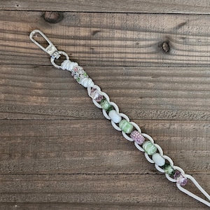 May include: White cord with a silver clasp and green and pink beads.