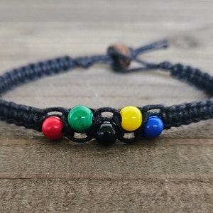 May include: A black braided bracelet with five colorful beads. The beads are red, green, black, yellow, and blue.