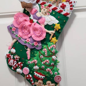 Könnte beinhalten: Ein grüner Weihnachtssocken mit einer Filzfee, die einen Sternenzauberstab hält. Der Socken ist mit Zuckerstangen, Lebkuchenmännern, Cupcakes und dem Namen "Mia" verziert.