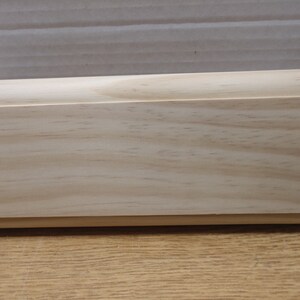 May include: A close-up of a light wood shelf with a smooth, slightly rounded edge. The shelf is made of unfinished pine wood and has a natural grain pattern.
