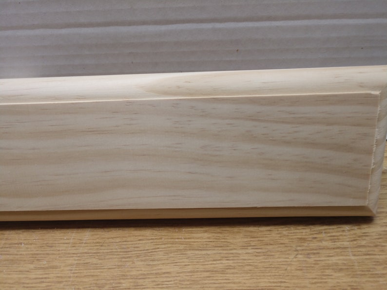 May include: A close-up of a light wood shelf with a smooth, slightly rounded edge. The shelf is made of unfinished pine wood and has a natural grain pattern.