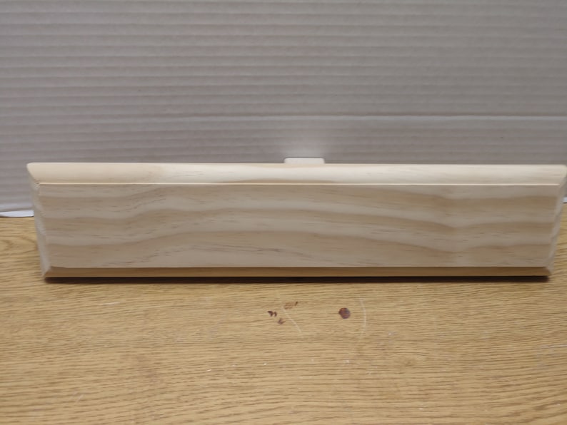 May include: A plain, unfinished wooden plaque with a slightly rounded edge. The plaque is made of light-colored wood with a natural grain pattern.