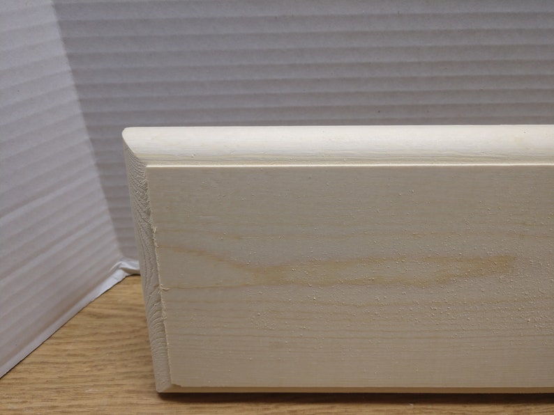 May include: A close-up of a plain, unfinished, white wood board. The board has a slightly rounded edge and a smooth surface.