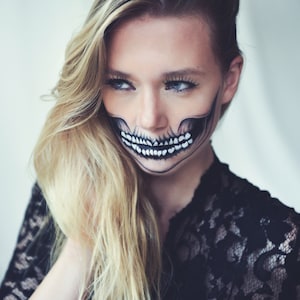May include: A woman with long blonde hair wearing a black lace top has a skull painted on her face. The skull is black and white with a white smile.