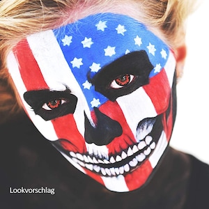 May include: A person with a skull face painted in red, white, and blue, resembling the American flag. The person has red contact lenses.