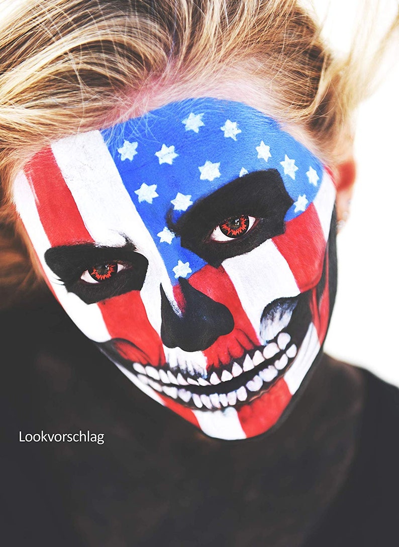 May include: A person with a skull face painted in red, white, and blue, resembling the American flag. The person has red contact lenses.