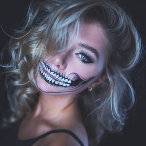 May include: A woman with blonde hair and a skeleton face paint, looking over her shoulder with a mischievous smile.