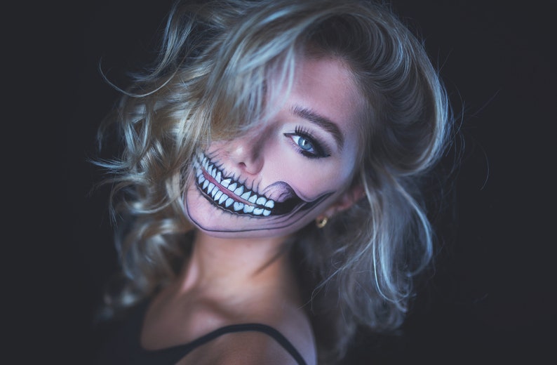 May include: A woman with blonde hair and a skeleton face paint, looking over her shoulder with a mischievous smile.