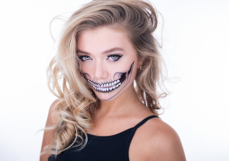 May include: A woman with blonde hair and a skull makeup design on her face. She is wearing a black tank top.