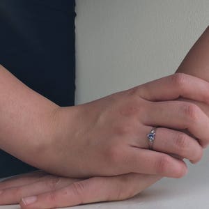K&ouml;nnte beinhalten: Ein silberner Ring mit einem blauen Edelstein, der in einer dreieckigen Form gefasst ist. Der Ring befindet sich an einem Finger.