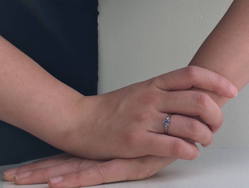 K&ouml;nnte beinhalten: Ein silberner Ring mit einem blauen Edelstein, der in einer dreieckigen Form gefasst ist. Der Ring befindet sich an einem Finger.
