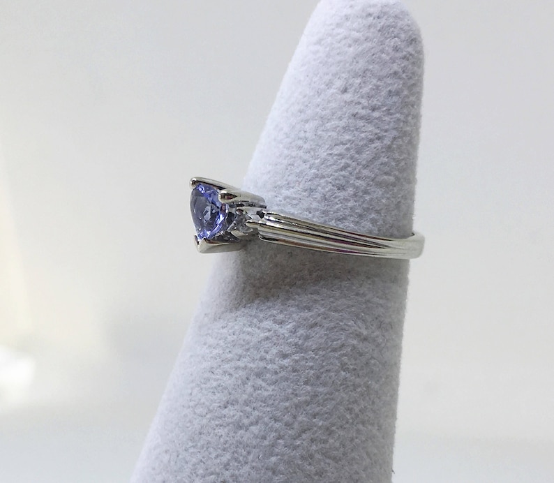 K&ouml;nnte beinhalten: Ein silberner Ring mit einem herzf&ouml;rmigen blauen Edelstein und kleineren klaren Edelsteinen auf der Ringschiene.