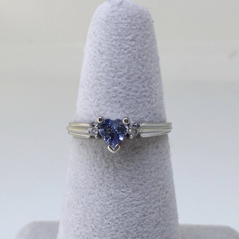 K&ouml;nnte beinhalten: Ein silberner Ring mit einem herzf&ouml;rmigen blauen Edelstein und zwei kleineren klaren Edelsteinen auf der Ringschiene.