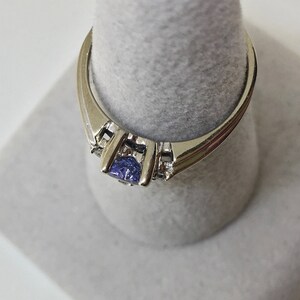 K&ouml;nnte beinhalten: Ein silberner Ring mit einem blauen Edelstein und kleineren klaren Edelsteinen auf der Ringschiene.