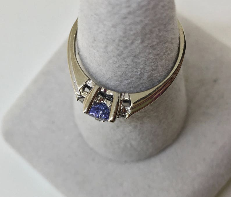 K&ouml;nnte beinhalten: Ein silberner Ring mit einem blauen Edelstein und kleineren klaren Edelsteinen auf der Ringschiene.