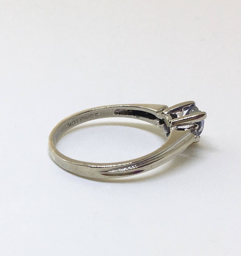 K&ouml;nnte beinhalten: Ein silberner Ring mit einem klaren Edelstein, der in einer Krappenfassung sitzt. Der Ring ist innen mit "10K" gekennzeichnet.