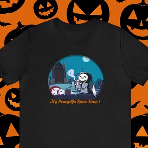 Puede incluir: Camiseta negra con una imagen de dibujos animados de un esqueleto sosteniendo una taza de café en un cementerio. El texto "It's Pumpkin Spice Time!" está impreso debajo de la imagen.