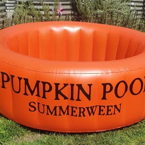 May include: An inflatable orange Pumpkin Pool for Summerween. The pool is round and has the words "PUMPKIN POOL" and "SUMMERWEEN" printed in black on the side. It is sitting on green grass.