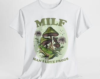May include: White t-shirt with a green frog sitting on a mushroom. The shirt has the text "MILF MAN I LOVE FROGS" printed on it.
