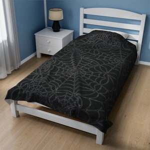 May include: A black twin-sized bedspread with a silver spiderweb design. The bedspread is on a white bed frame in a room with blue walls and a white nightstand. A black lamp sits on the nightstand.