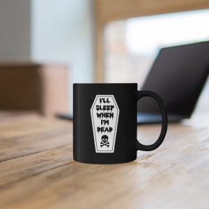May include: Black coffee mug with a white graphic of a coffin with the text "I'll sleep when I'm dead" and a skull and crossbones.