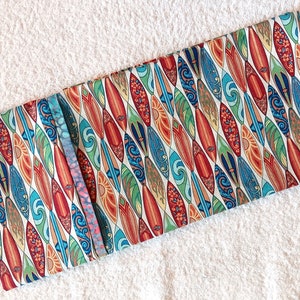 May include: A white fabric with a repeating pattern of colorful surfboards. The surfboards are decorated with floral and wave designs.