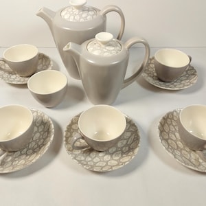 May include: A grey ceramic tea set with a white interior, featuring two teapots, a creamer, and six cups with saucers. The saucers have a grey and white pattern. The set is designed for serving tea.