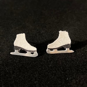 以下が含まれることがあります： 銀製のスケートのイヤリングのペア。スケートは白で、黒いブレードが付いており、キラキラとした仕上げになっています。