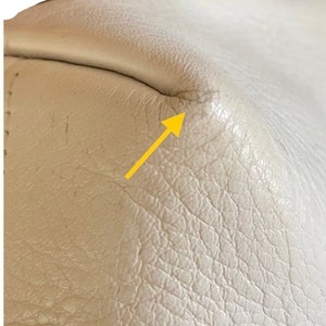 May include: Close-up of a white leather surface with a small crease in the corner. The leather has a textured grain.