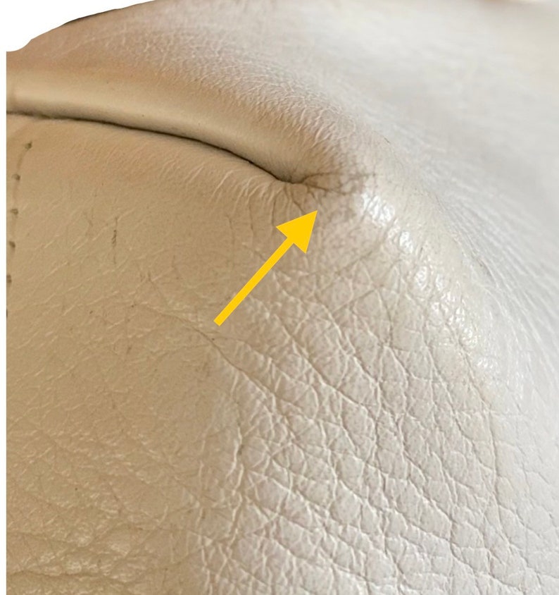 May include: Close-up of a white leather surface with a small crease in the corner. The leather has a textured grain.