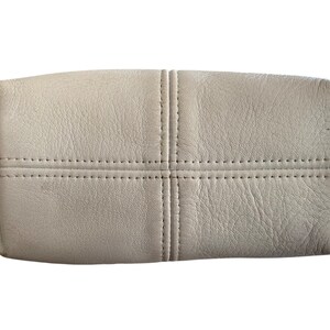 May include: A light gray leather handbag with a stitched design. The bag has a rectangular shape and a smooth, textured surface.
