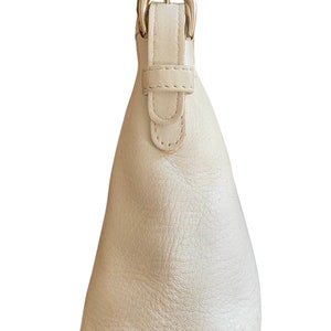 May include: A white leather handbag with a silver buckle closure. The bag has a simple, classic design.