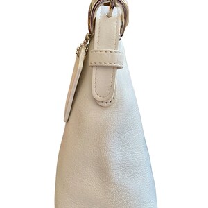 May include: A white leather handbag with a silver buckle and strap. The bag has a small, rectangular pocket on the front.