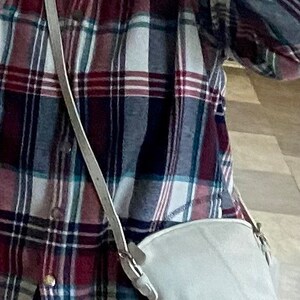 May include: A white crossbody bag with a long strap worn over a red, white, and blue plaid shirt.