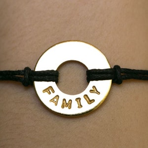 May include: A black cord bracelet with a gold-colored metal circle charm that says "FAMILY" in raised letters.