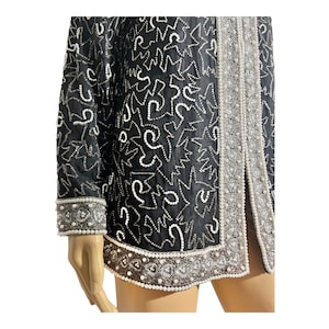 May include: Black jacket with white and silver embellishments. The jacket features a pattern of white shapes and is trimmed with silver and white beads. The cuffs and edges are detailed with intricate beadwork, creating a glamorous look.